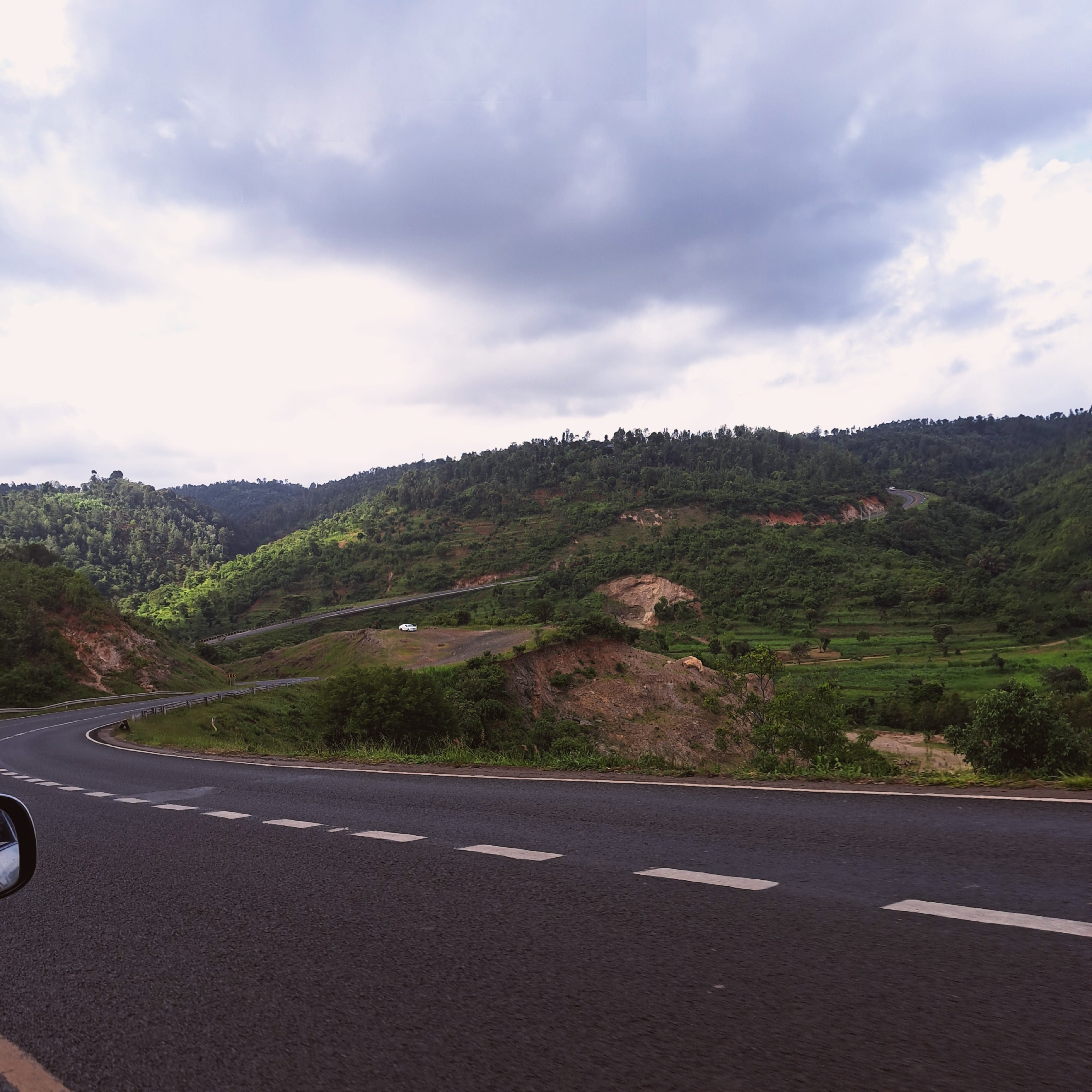 Winding asphalt road curving through lush green hills under a cloudy sky capturing the serene, fertile landscapes that reflect East Africa’s coffee‑growing regions.